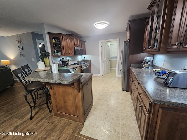 kitchen with appliances with stainless steel finishes, a kitchen breakfast bar, kitchen peninsula, and dark brown cabinets