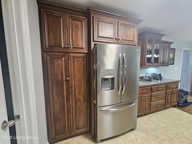 kitchen with light tile patterned flooring, light stone countertops, dark brown cabinetry, and stainless steel fridge with ice dispenser