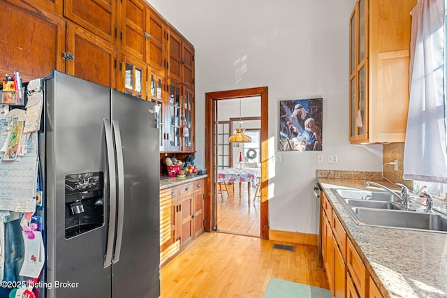 kitchen featuring stainless steel refrigerator with ice dispenser, light hardwood / wood-style floors, sink, and light stone counters