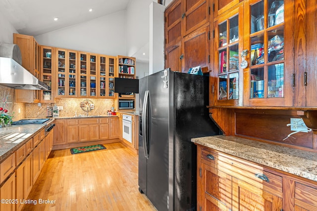 kitchen with appliances with stainless steel finishes, range hood, lofted ceiling, backsplash, and light stone counters