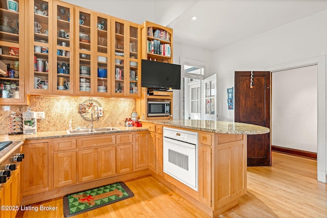 kitchen featuring sink, oven, backsplash, light stone countertops, and light hardwood / wood-style flooring