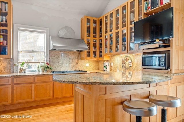 kitchen featuring lofted ceiling, appliances with stainless steel finishes, a kitchen breakfast bar, light stone countertops, and decorative backsplash