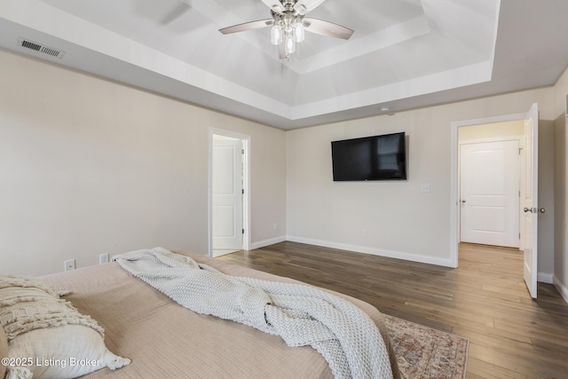 bedroom featuring ceiling fan, wood-type flooring, and a tray ceiling