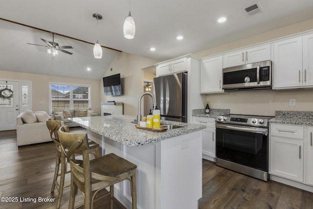 kitchen featuring appliances with stainless steel finishes, white cabinetry, a kitchen bar, a kitchen island with sink, and light stone countertops