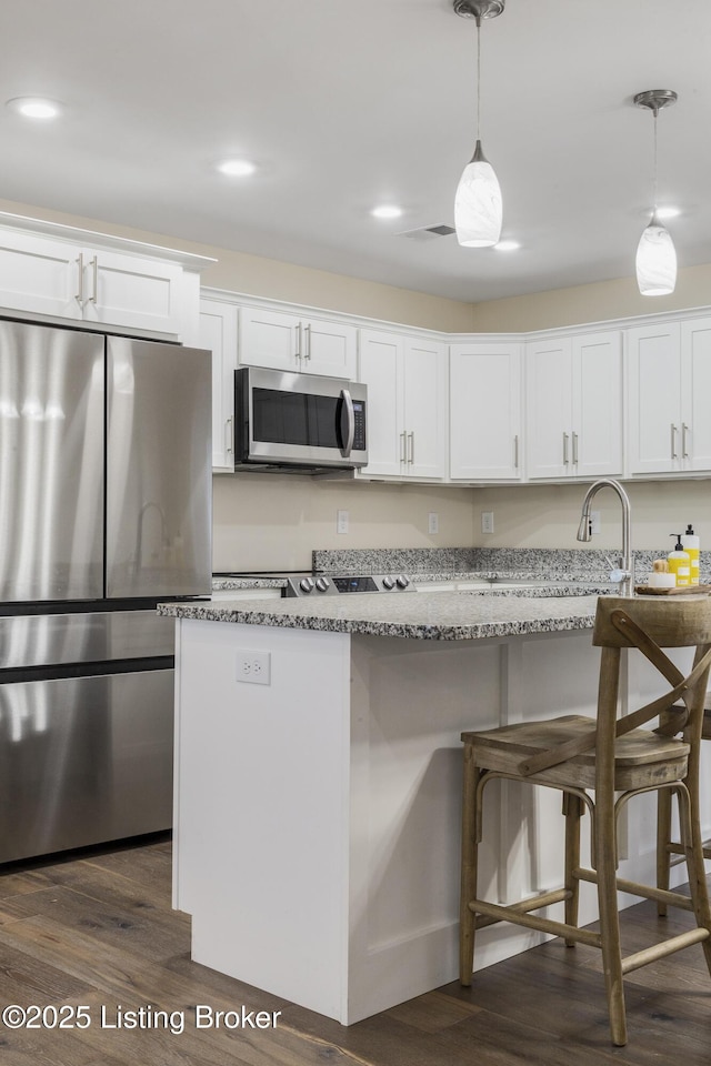 kitchen with hanging light fixtures, white cabinetry, appliances with stainless steel finishes, and light stone countertops