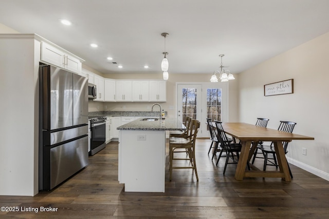 kitchen featuring sink, appliances with stainless steel finishes, dark stone countertops, white cabinetry, and a center island with sink