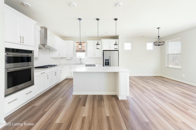 kitchen featuring a kitchen island, wall chimney range hood, light countertops, appliances with stainless steel finishes, and a sink