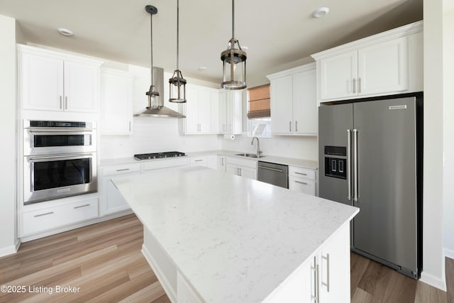 kitchen featuring light wood-style flooring, a sink, white cabinetry, appliances with stainless steel finishes, and wall chimney exhaust hood