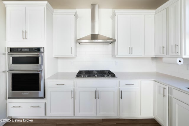 kitchen featuring tasteful backsplash, white cabinets, stainless steel appliances, light stone countertops, and wall chimney exhaust hood