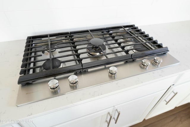 details with tasteful backsplash, light stone countertops, stainless steel gas cooktop, and white cabinets