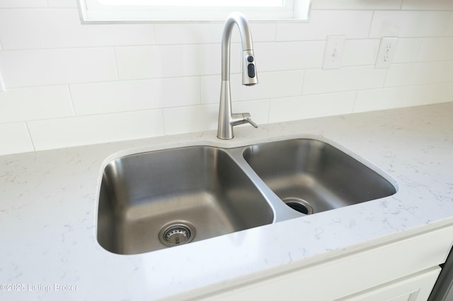 room details with sink, backsplash, light stone countertops, and white cabinets