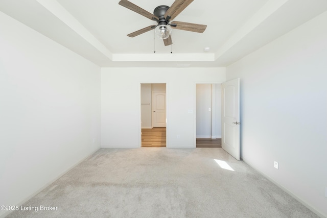 unfurnished bedroom with ceiling fan, light colored carpet, and a raised ceiling