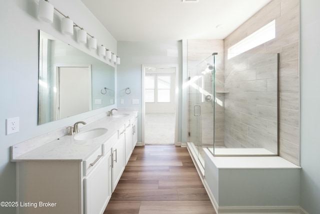 full bathroom featuring double vanity, wood finished floors, a stall shower, and a sink