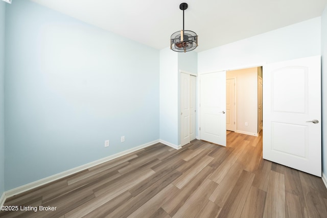 unfurnished bedroom featuring hardwood / wood-style flooring, a notable chandelier, and a closet