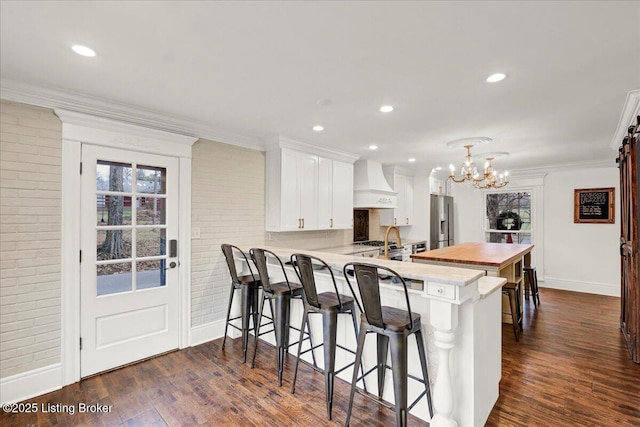 kitchen featuring high quality fridge, kitchen peninsula, custom range hood, brick wall, and white cabinets