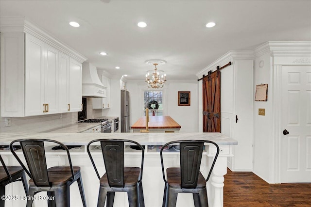 kitchen with pendant lighting, a breakfast bar area, appliances with stainless steel finishes, custom range hood, and a barn door