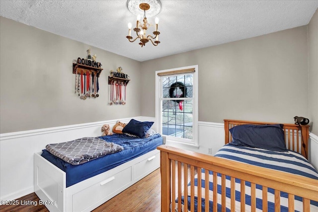 bedroom with hardwood / wood-style flooring, a textured ceiling, and a notable chandelier