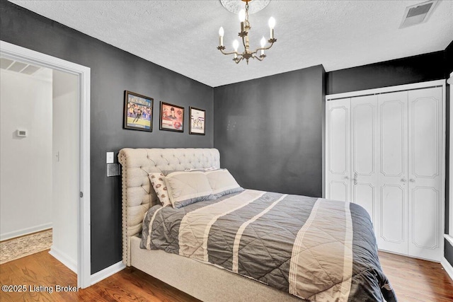 bedroom with hardwood / wood-style floors, a notable chandelier, a textured ceiling, and a closet