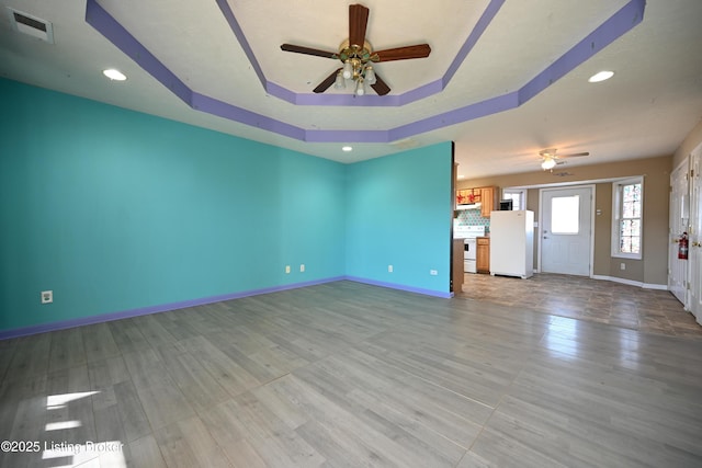 unfurnished living room featuring ceiling fan, a raised ceiling, and light hardwood / wood-style flooring