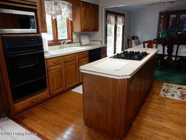 kitchen featuring sink, light wood-type flooring, black appliances, and a kitchen island