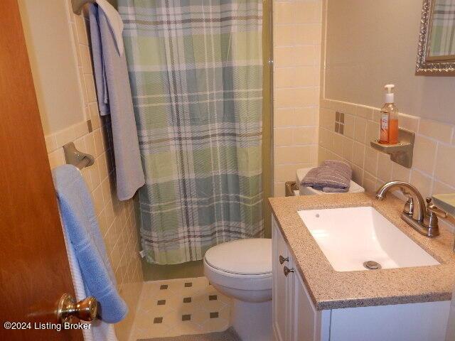 bathroom featuring walk in shower, vanity, toilet, and tile walls