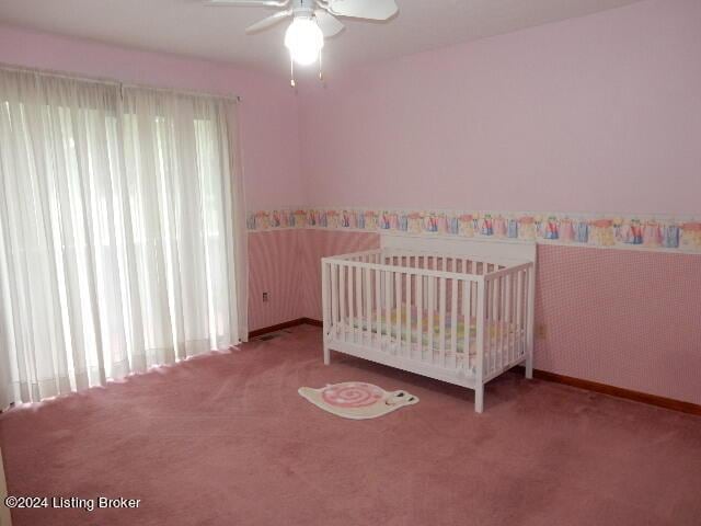 unfurnished bedroom featuring a nursery area, ceiling fan, and carpet