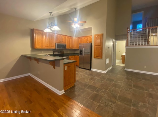 kitchen featuring pendant lighting, high vaulted ceiling, a kitchen bar, kitchen peninsula, and stainless steel appliances