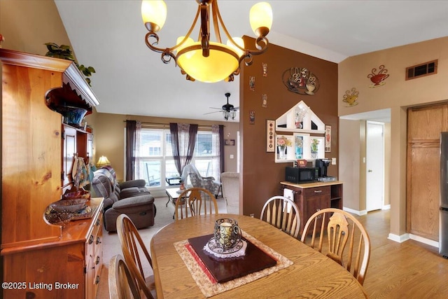 dining area with high vaulted ceiling, ceiling fan with notable chandelier, and light wood-type flooring