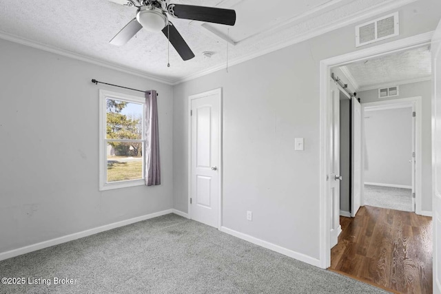 unfurnished bedroom with ceiling fan, ornamental molding, a barn door, and a textured ceiling