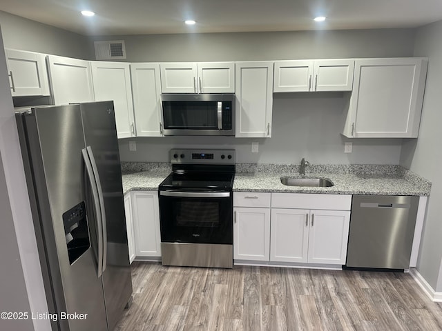 kitchen with light stone counters, appliances with stainless steel finishes, sink, and white cabinets