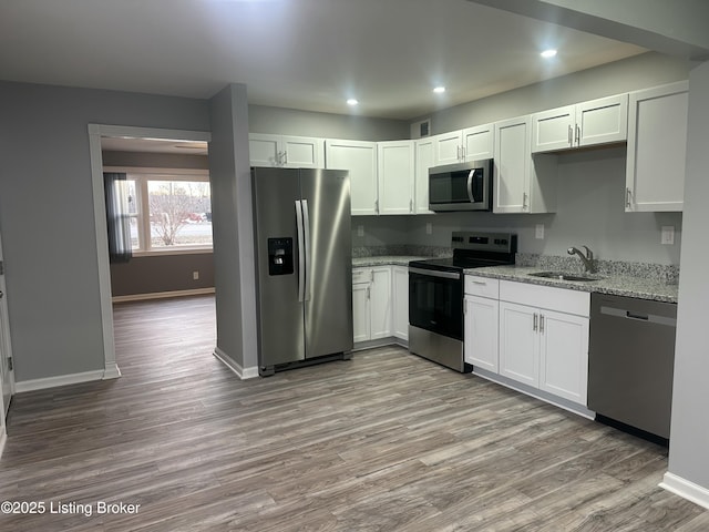 kitchen with light stone countertops, white cabinetry, appliances with stainless steel finishes, and sink