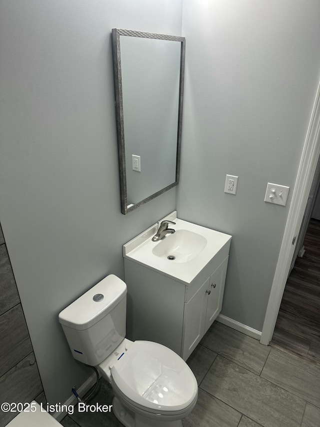 half bathroom featuring baseboards, vanity, and toilet