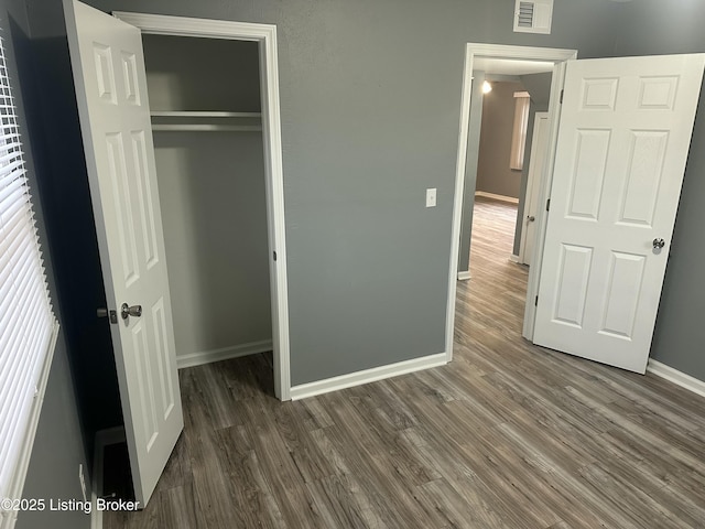 unfurnished bedroom featuring a closet, visible vents, baseboards, and wood finished floors