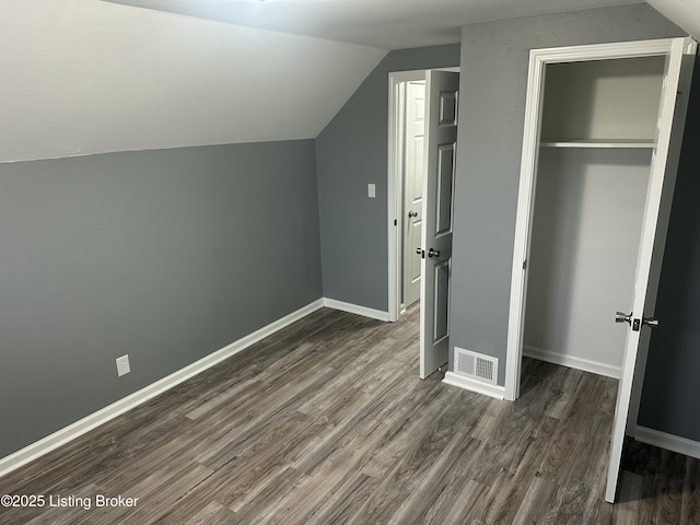 unfurnished bedroom with baseboards, visible vents, lofted ceiling, dark wood-type flooring, and a closet