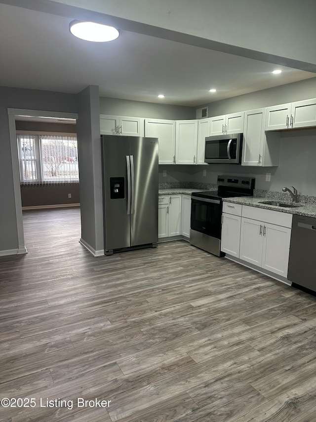 kitchen featuring dark wood finished floors, appliances with stainless steel finishes, white cabinets, a sink, and light stone countertops