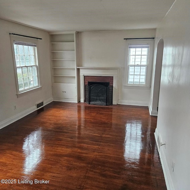 unfurnished living room with dark hardwood / wood-style floors, a wealth of natural light, built in features, and a fireplace