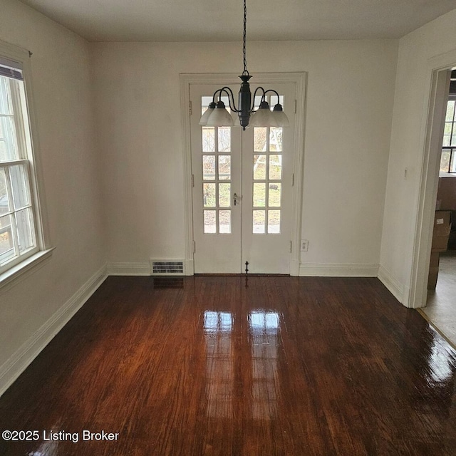 unfurnished dining area with dark hardwood / wood-style floors, a notable chandelier, and french doors