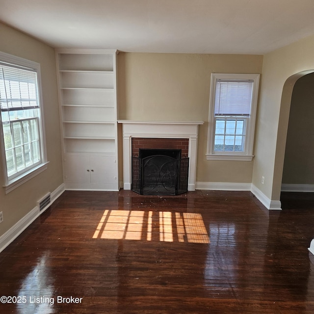 unfurnished living room with arched walkways, dark wood finished floors, a fireplace, visible vents, and baseboards