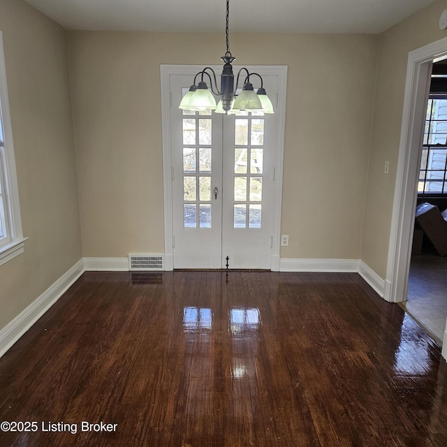 unfurnished dining area with dark wood-type flooring, an inviting chandelier, visible vents, and baseboards