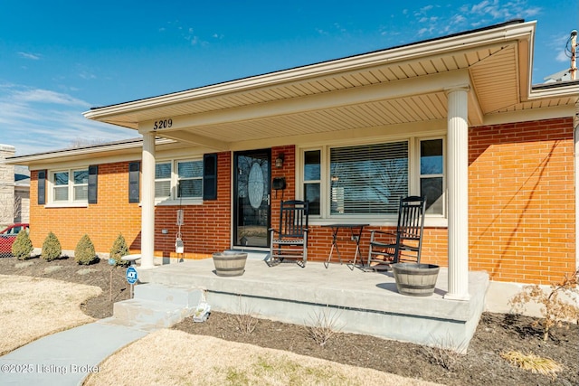 view of exterior entry with a porch and brick siding