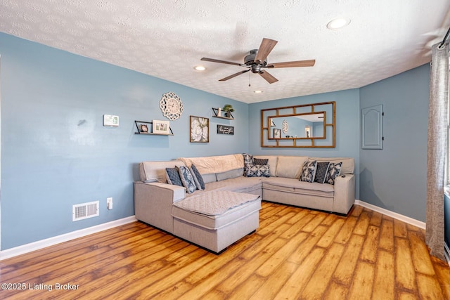 living area with a textured ceiling, light wood-style flooring, visible vents, and baseboards