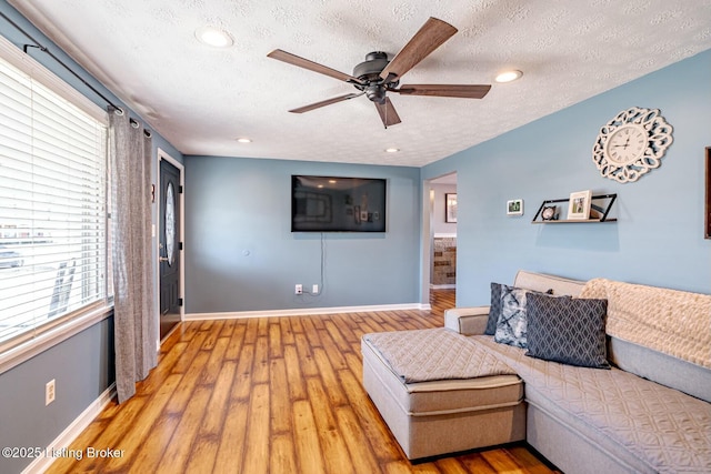 living area featuring light wood finished floors, baseboards, a ceiling fan, a textured ceiling, and recessed lighting