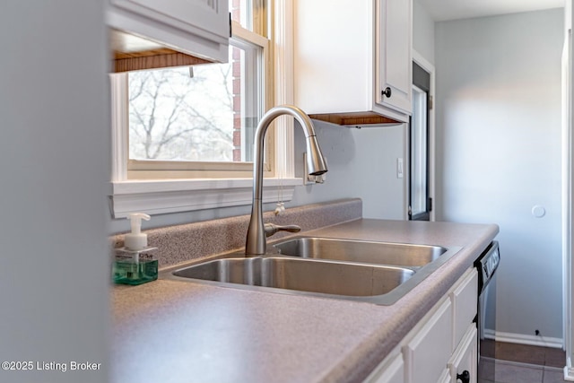 kitchen with black dishwasher, light countertops, a sink, and white cabinetry