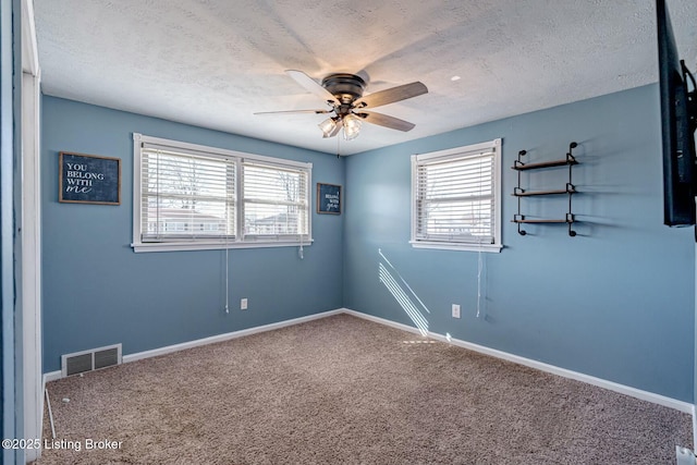 carpeted spare room featuring a textured ceiling, a wealth of natural light, and visible vents