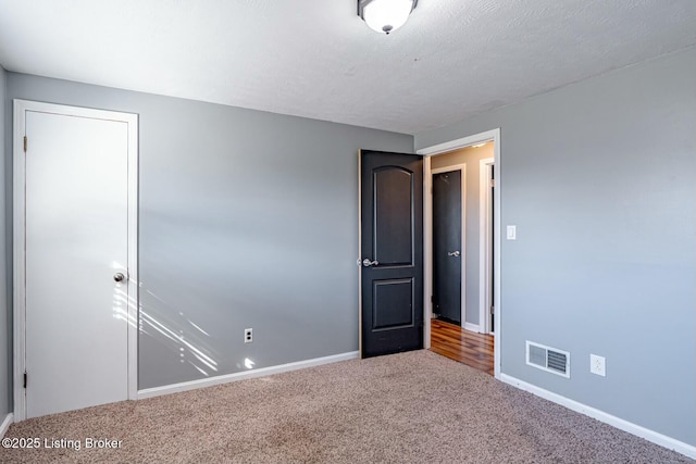 spare room featuring carpet floors, visible vents, a textured ceiling, and baseboards