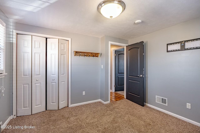 unfurnished bedroom featuring a textured ceiling, light colored carpet, visible vents, baseboards, and a closet