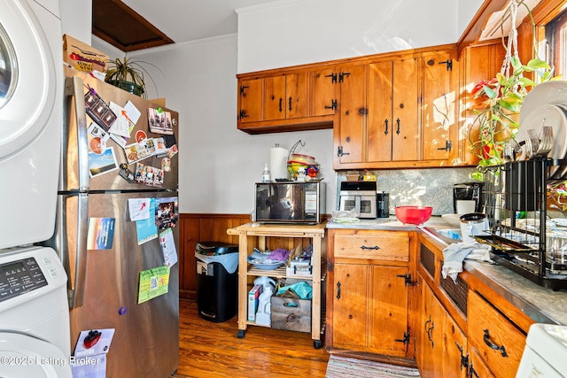 kitchen featuring stainless steel refrigerator, dark hardwood / wood-style floors, stacked washer and clothes dryer, tasteful backsplash, and ornamental molding