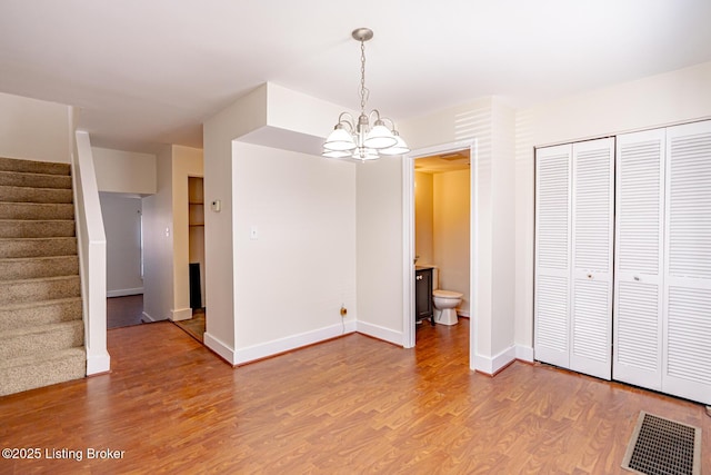 unfurnished dining area featuring a chandelier, wood finished floors, visible vents, baseboards, and stairway