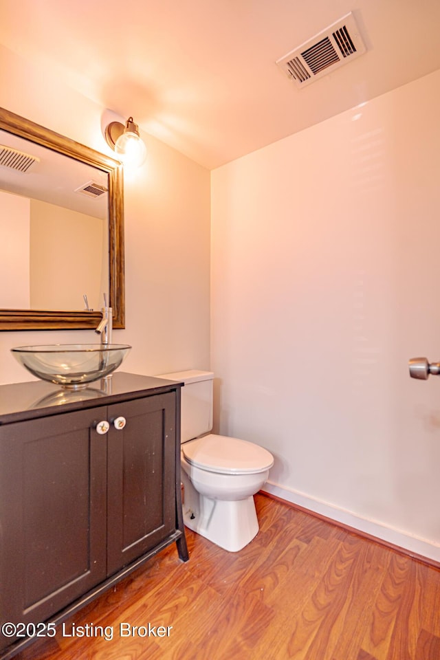 half bathroom featuring visible vents, toilet, vanity, wood finished floors, and baseboards