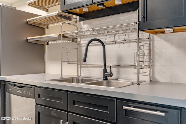 kitchen featuring tasteful backsplash, dishwasher, dark cabinetry, open shelves, and a sink